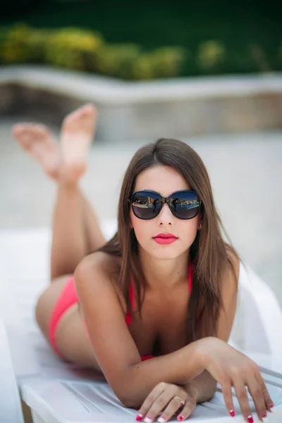 Hermosa dama en gafas de sol se encuentra en un más largo frente a la piscina —  Fotos de Stock