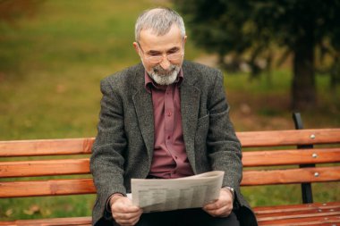 Gri ceketli güzel sakallı güzel Dede parkta bir bankta oturur ve bir gazete okuyor