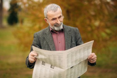 Gri ceketli güzel sakallı güzel dede parkta stand ve bir gazete okuyor