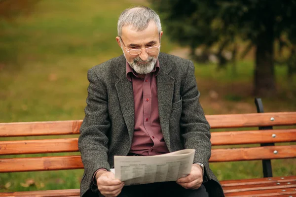 Gri ceketli güzel sakallı güzel Dede parkta bir bankta oturur ve bir gazete okuyor