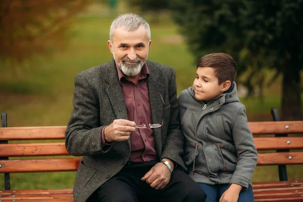 Děda a vnuk spolu strávit čas v parku. Sedí na lavičce. Procházky v parku a radosti — Stock fotografie