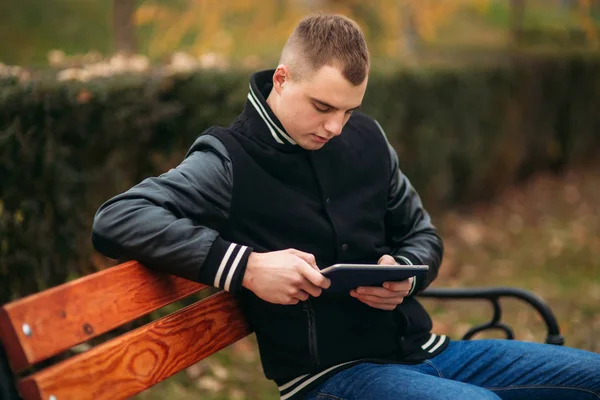 Egy fiatal srác egy fekete kabát használ egy tabletta — Stock Fotó