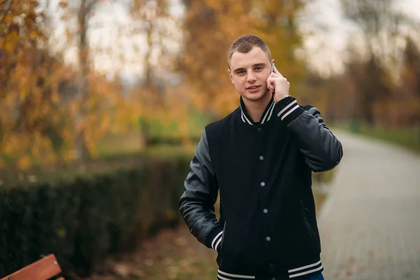 Un joven con una chaqueta negra usa el teléfono — Foto de Stock