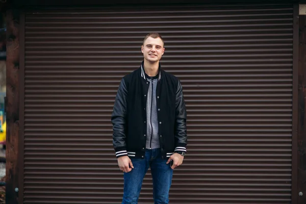 Un joven con una chaqueta negra sobre un fondo de pared de rayas oscuras — Foto de Stock