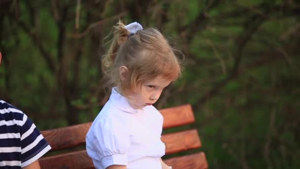 Boy eating an ice cream and sitting on the bench while girl is looking — Stock Video