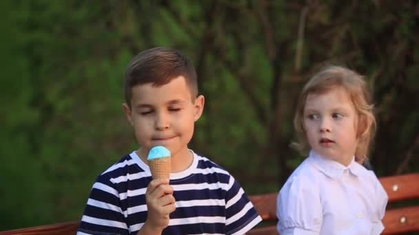 Pojken äter en glass och sitta på bänken medan tjej söker — Stockvideo