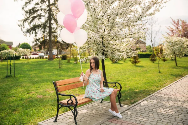 Kız bir bankta oturur ve pembe helyum topları tutmak — Stok fotoğraf