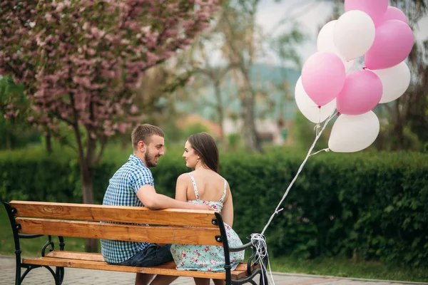 Paar sitzt auf einer Bank und hält rosa Heliumkugeln in der Hand — Stockfoto