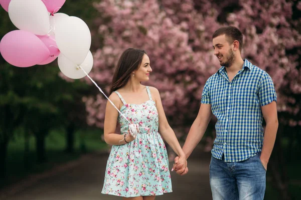 Junges glückliches Paar verliebt im Freien. schöner Mann und schöne Frau bei einem Spaziergang in einem frühlingshaft blühenden Park. sie halten Heliumkugeln — Stockfoto