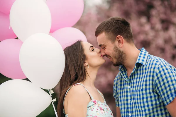 Junges glückliches Paar verliebt im Freien. schöner Mann und schöne Frau bei einem Spaziergang in einem frühlingshaft blühenden Park. sie halten Heliumkugeln — Stockfoto