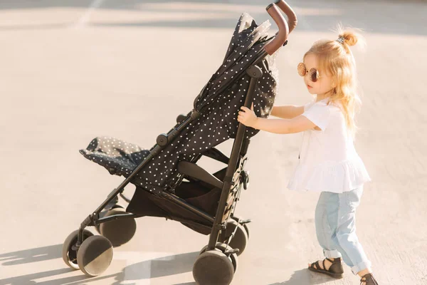 Una niña está empujando su carruaje de bebé — Foto de Stock