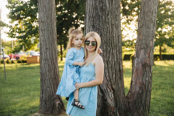 Young beautiful woman with her little cute daughter. Young daughter hugs mother in summer park — Stock Photo, Image