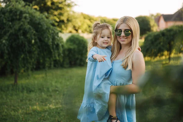 Giovane bella donna con la sua piccola figlia carina. Giovane figlia abbraccia la madre nel parco estivo — Foto Stock