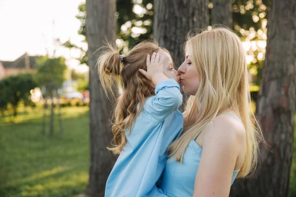 Joven mujer hermosa con su pequeña hija linda. hija joven abraza a la madre en el parque de verano —  Fotos de Stock