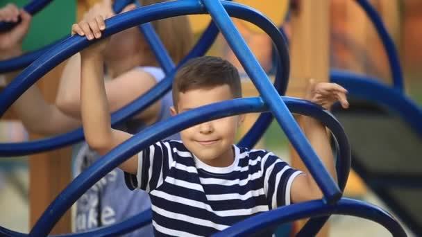Un bambino con una maglietta a righe sta giocando nel parco giochi, oscillando su un'altalena.Primavera, tempo soleggiato — Video Stock
