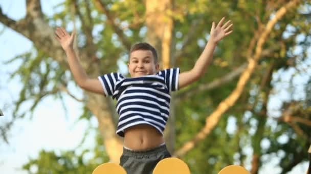 स्ट्रिप टी-शर्टमध्ये एक लहान मुलगा खेळाच्या मैदानावर खेळत आहे, स्विंगवर स्विंग करीत आहे. स्प्रिंग, सनी हवामान — स्टॉक व्हिडिओ