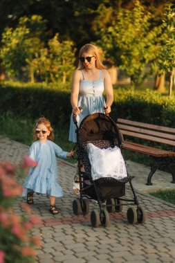 küçük kızı anne bebek arabası itme yardımcı olur. Mutlu bir aile