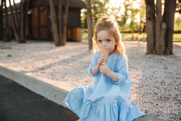 Hermosa niña en un vestido azul comiendo un helado — Foto de Stock