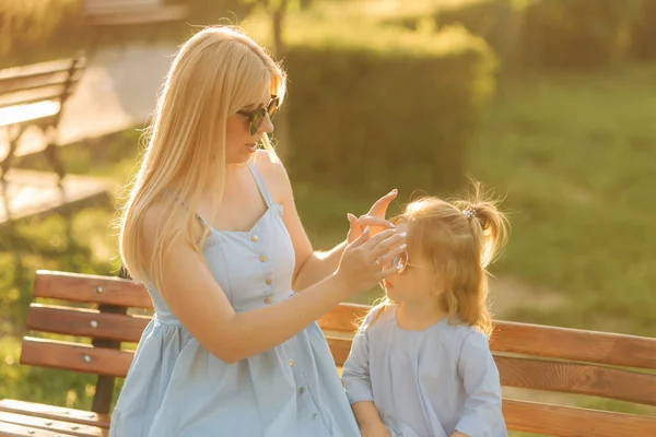 Maminka a jeho malá dcera sedí na lavičce v parku — Stock fotografie