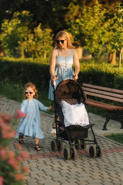 küçük kızı anne bebek arabası itme yardımcı olur. Mutlu bir aile