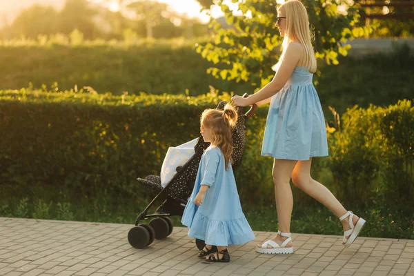 Lilla dotter hjälper mamma push barnvagn. Lycklig familj — Stockfoto
