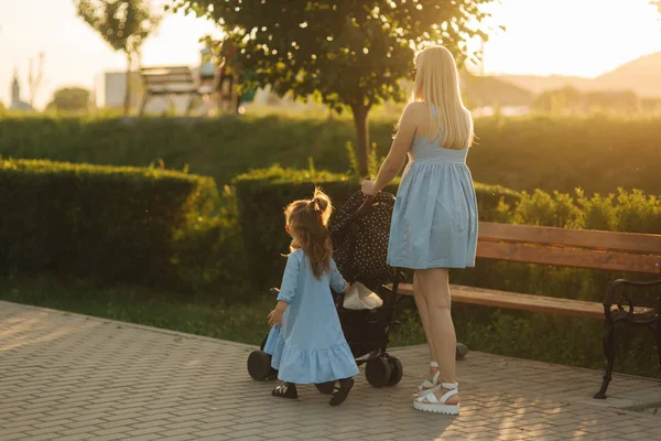 küçük kızı anne bebek arabası itme yardımcı olur. Mutlu bir aile