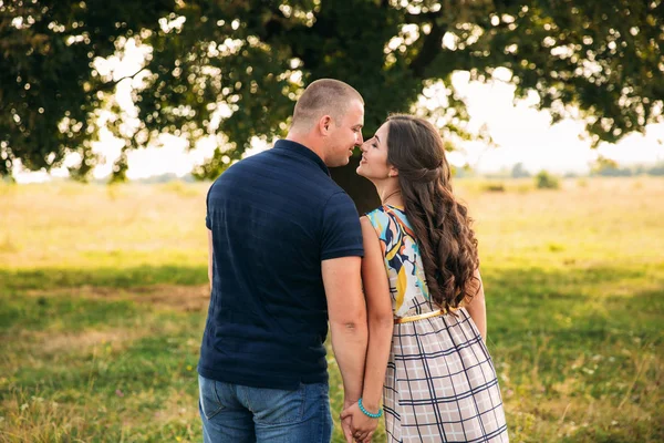 Handsome guy and an attractive girl kiss each other near a large green tree. Love story — Stock Photo, Image