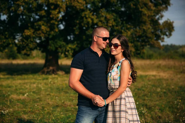 Snygg kille och en attraktiv tjej krama varandra nära ett stort grönt träd. Kärlekshistoria — Stockfoto