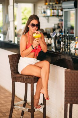 Çekici kız plaj bar üzerinde dinlenme ferahlatıcı bir kokteyl içki. Parlak mayolar ve güneş gözlüğü