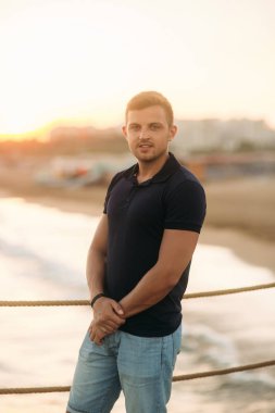 Yakışıklı adam deniz kenarında iskelede günbatımı zamanında ayakta