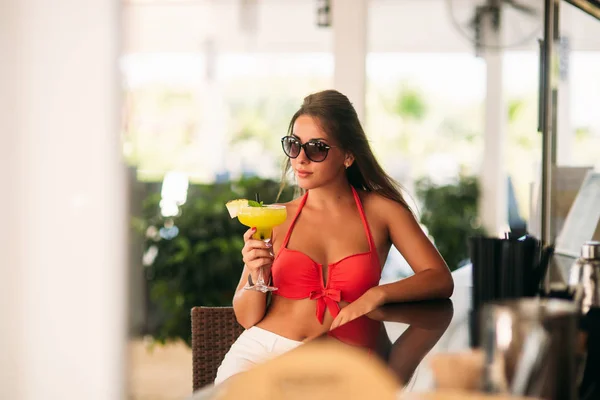 Vonzó lány nyugszik a strand bárjában, igyon egy frissítő koktélt. A világos fürdőruhák és a napszemüveg — Stock Fotó