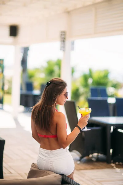 Gyönyörű fiatal nő visel fürdőruhát, ivás, egy színes koktél ül egy légiutas-kísérő, a beach club bárban. Lenyűgöző lány neki italt a nyári idő — Stock Fotó
