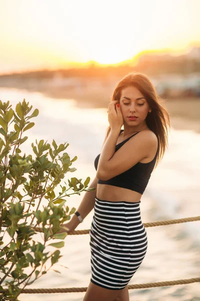 Menina atraente andando no cais perto do mar ao pôr do sol — Fotografia de Stock