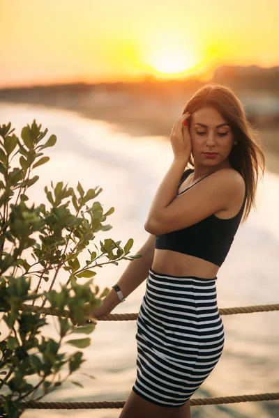 Attraktives Mädchen, das bei Sonnenuntergang auf einem Steg am Meer spaziert — Stockfoto
