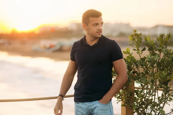 Handsome man standing on pier near the sea in sunset time