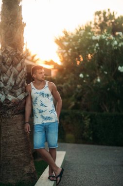 Gülümsüyor adam şort ve gömlek yaz aylarında park yakınlarında yürür