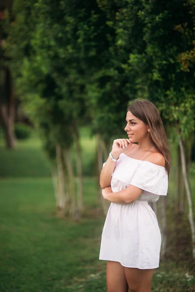 Fiatal és csinos lány, fehér ruhát a nyári város álló a fának a közelében — Stock Fotó