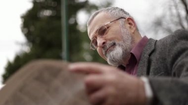 Gri ceketli güzel sakallı güzel Dede parkta bir bankta oturur ve bir gazete okuyor