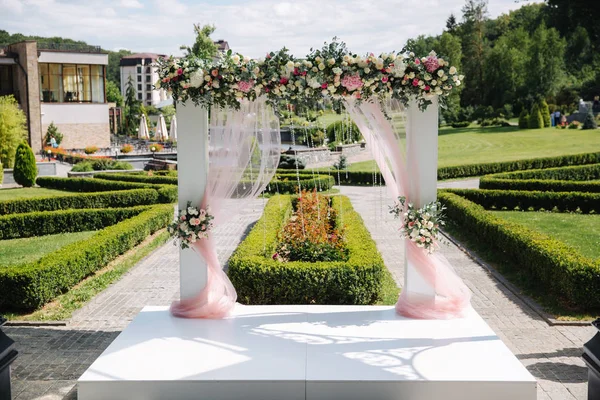 Свадебные украшения на открытом воздухе. Цветочный декор красивой белой арки. Вид на деревья — стоковое фото