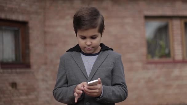 Handsome little Boy use his phone. Background of bick wall — Stock Video