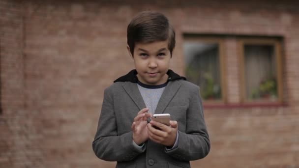 Le beau petit garçon utilise son téléphone. Fond de mur de brique — Video