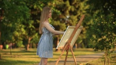 Güzel kız parkta ayakta ve boyalar ve bir spatula ile bir palet kullanarak resim çizer.