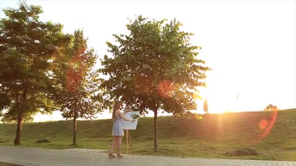 Όμορφο κορίτσι στέκεται στο πάρκο και τραβάει μια εικόνα χρησιμοποιώντας μια παλέτα με χρώματα και μια σπάτουλα. — Αρχείο Βίντεο