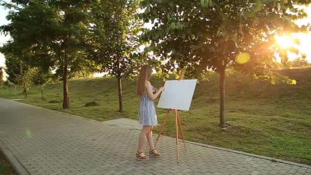 Beautiful girl artist is standing in the park and holding palette with paints — Stock Video