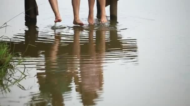 Mooie youn paar zitten op de pier in de buurt van het meer. splash door voeten maken Slow motion — Stockvideo