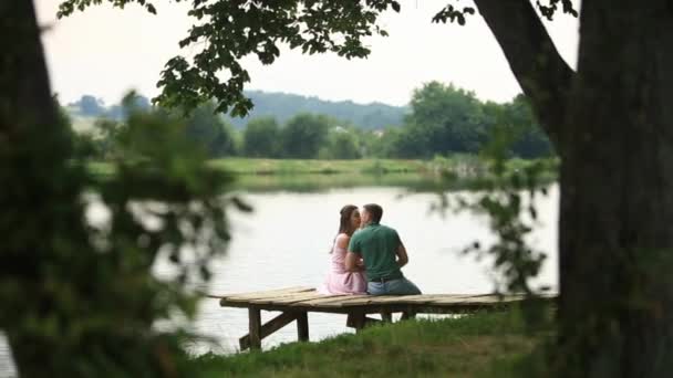 美しい若いカップルは、湖の近くの桟橋の上に座る。ロマンチックな雰囲気 — ストック動画