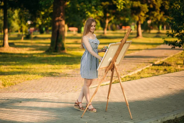 Блондинка в сукні малює картину в парку — стокове фото