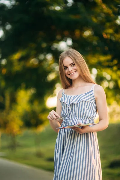 Hermosa artista chica está de pie en el parque y la celebración de la paleta con pinturas — Foto de Stock