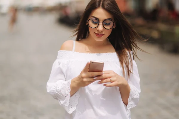 Atractivo sonriente joven mujer mensajes de texto en el teléfono celular al aire libre en la ciudad — Foto de Stock