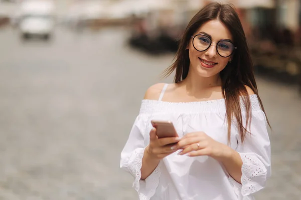 Atractivo sonriente joven mujer mensajes de texto en el teléfono celular al aire libre en la ciudad — Foto de Stock